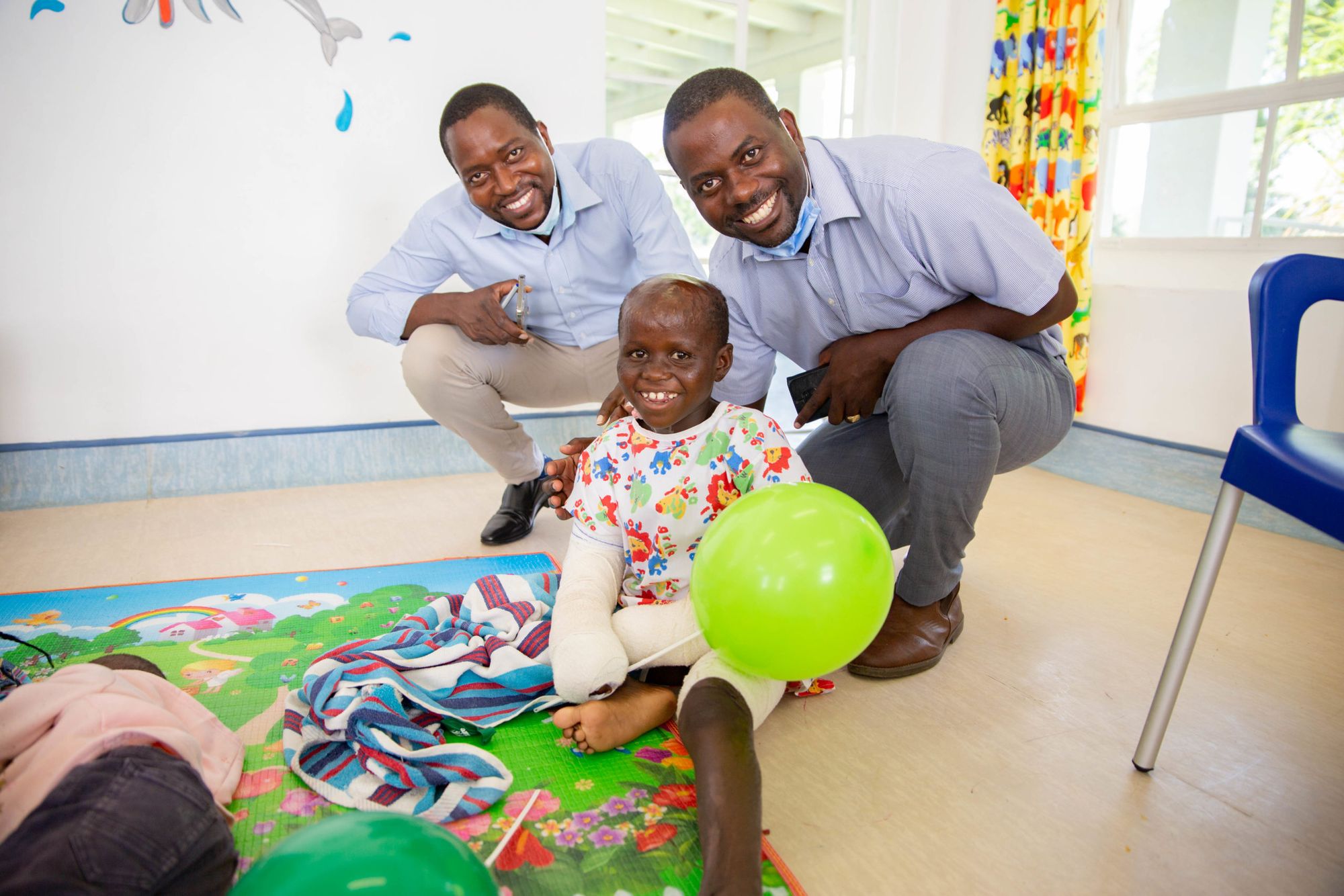 Two men smiling with child in a cast who is smiling